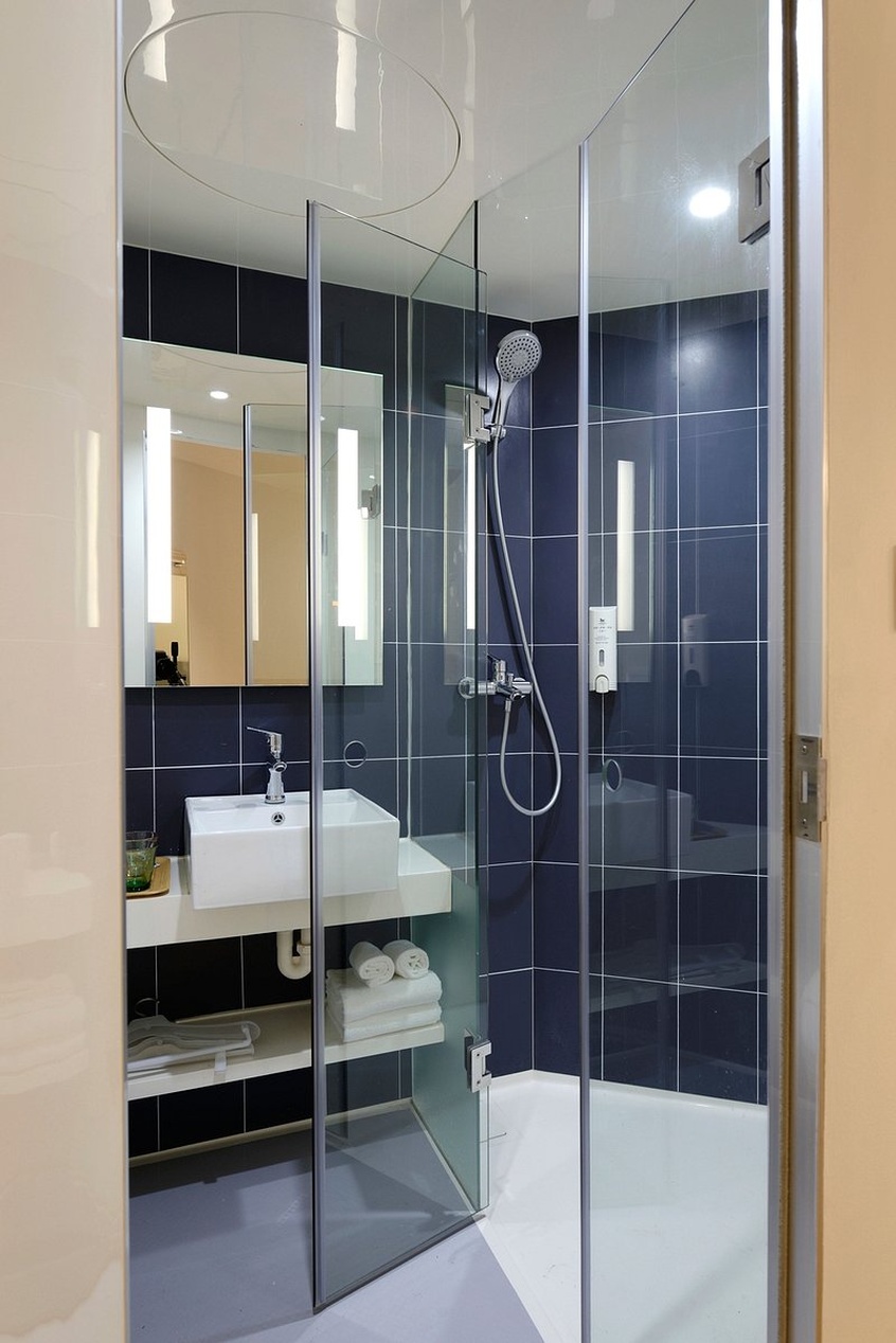 Een stijlvolle, compacte badkamer met donkerblauwe tegels, een zwevend wit meubel met open planken en ingebouwde nissen in de douche.